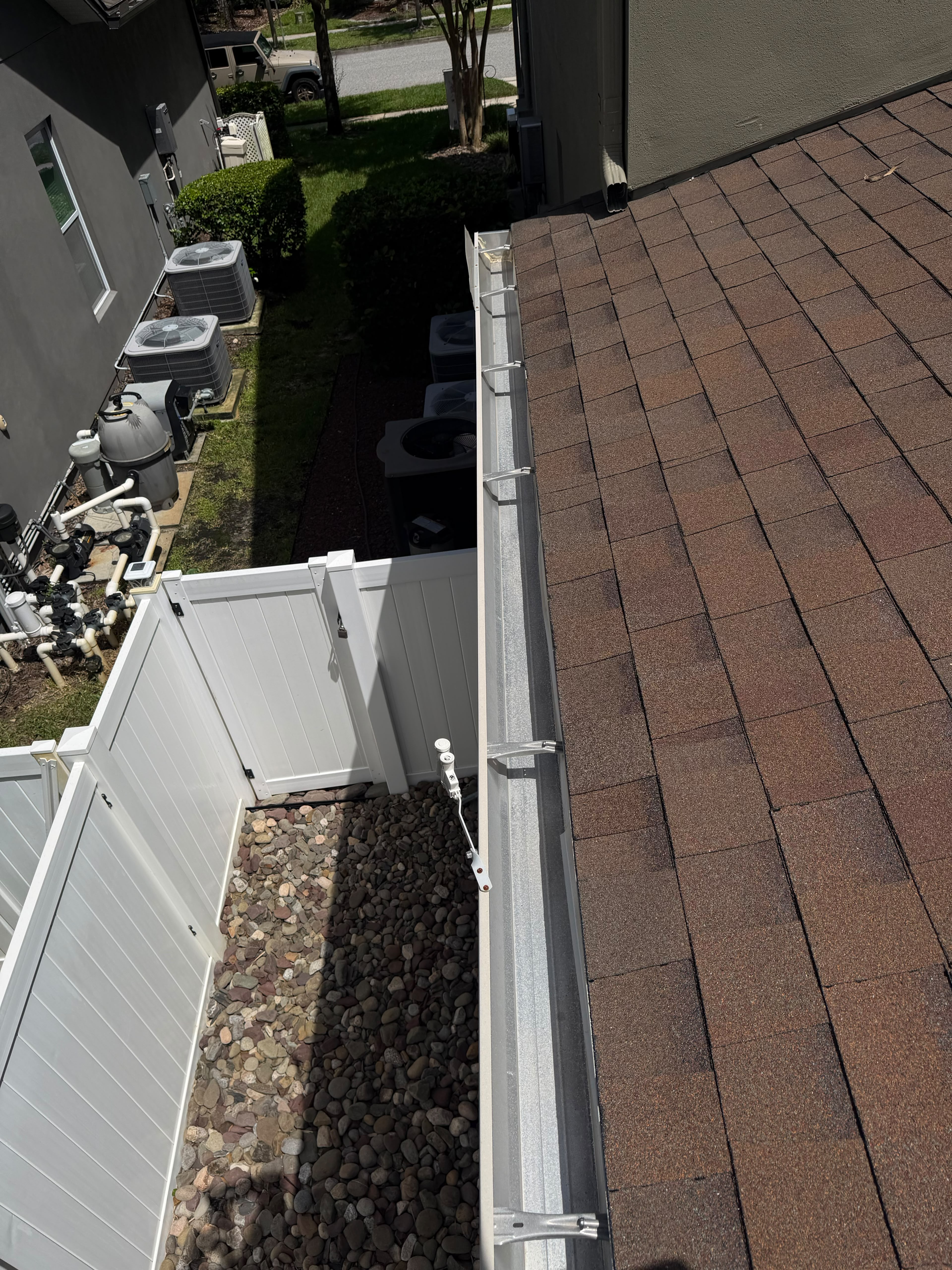 New seamless gutter installation along a residential roofline above a white fence